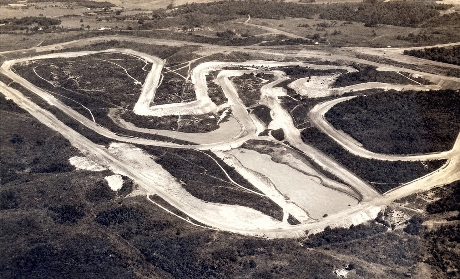 High-angle oblique aerial photograph from 1940 showing the newly excavated layout of the Autódromo de Interlagos in São Paulo, Brazil. The unpaved dirt contours of the full classic circuit—including the sweeping outer perimeter oval and the twisting infield sections—stand out in light soil against the surrounding undeveloped scrubland.